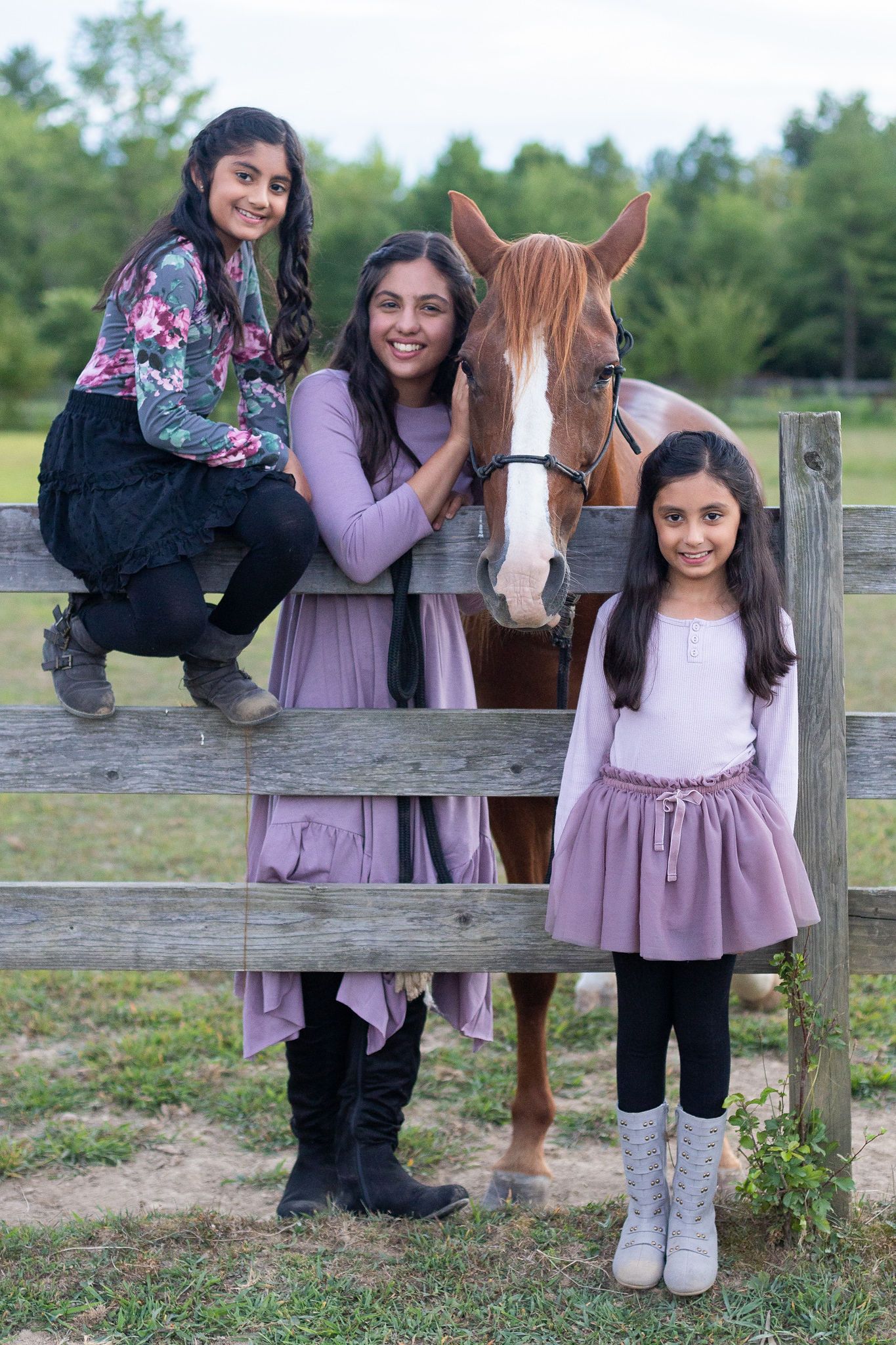 Three people and a chestnut horse pose at wooden fence in rural setting.
