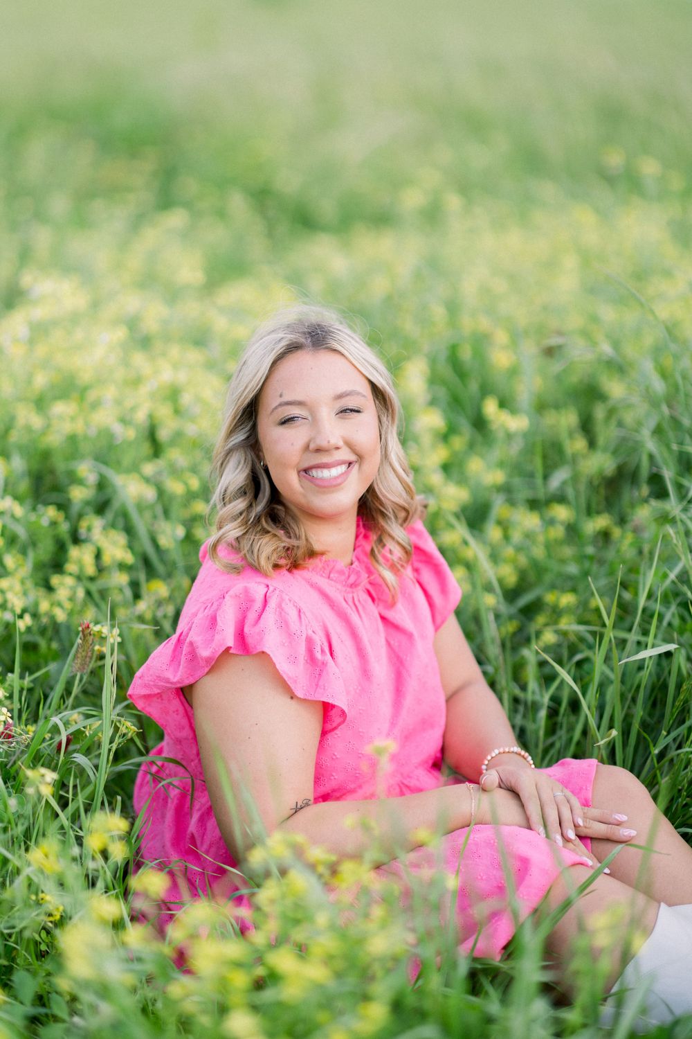Person in bright pink dress lying in green grass field with yellow flowers on sunny day.