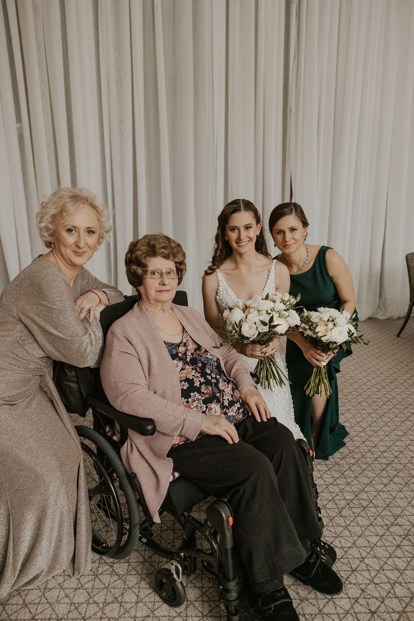Bride with bouquet poses with three generations of family including grandmother in wheelchair.