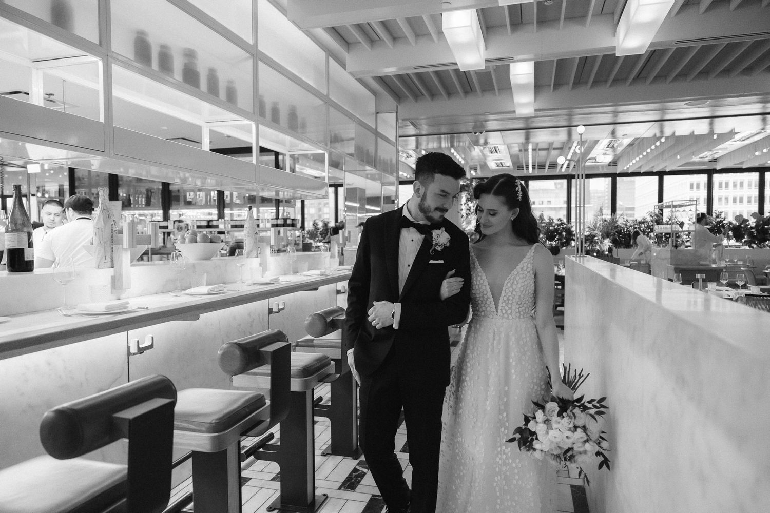Bride and groom walk together through elegant restaurant in black and white photo.