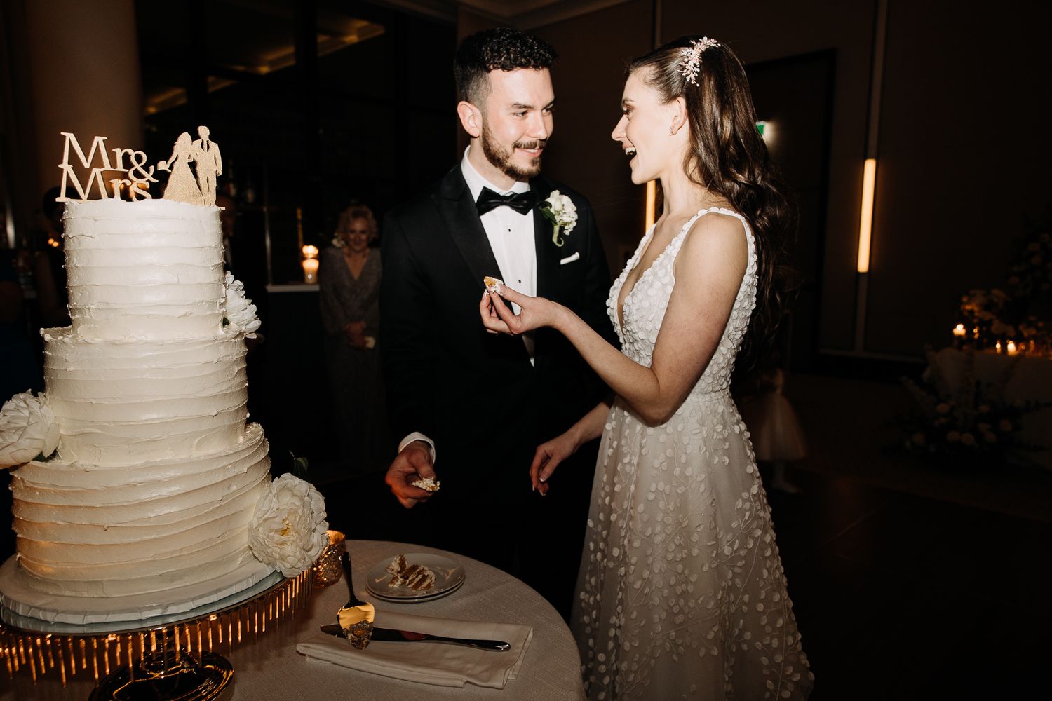 Bride and groom smile while cutting tall white multi-tiered wedding cake together.