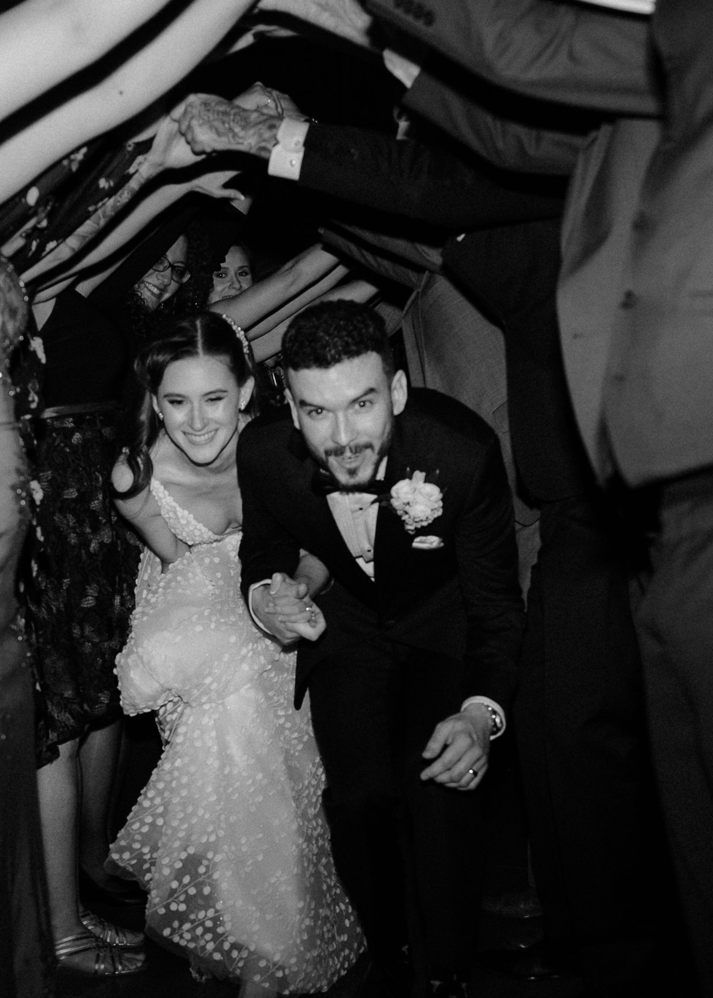 Black and white photo of joyful bride and groom making grand entrance through cheering wedding guests.