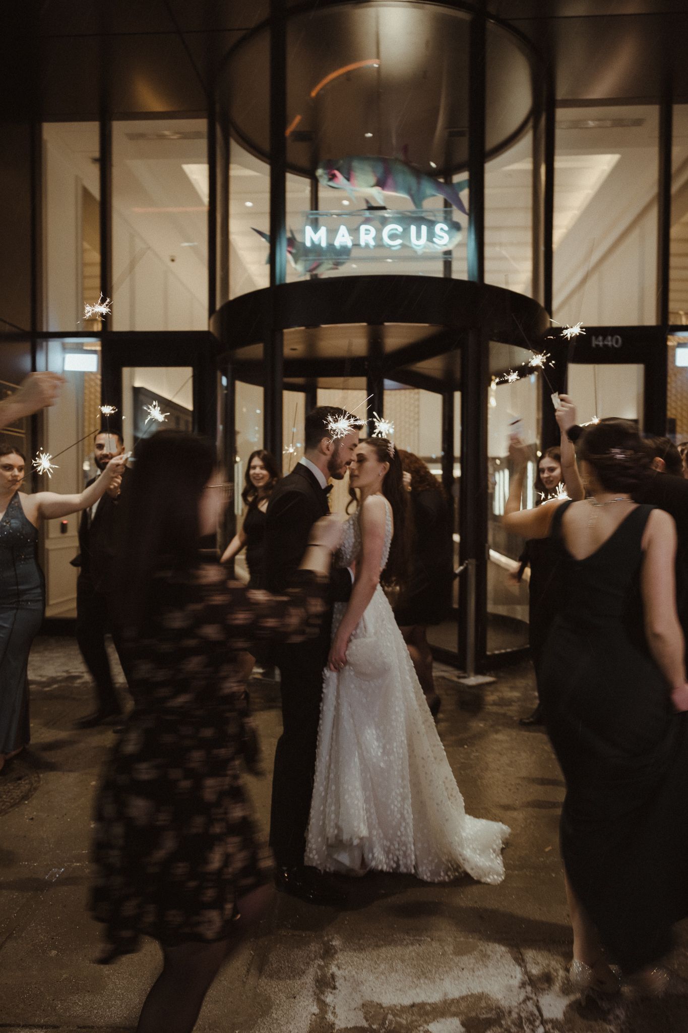 Bride and groom share a kiss surrounded by sparklers outside the Marcus hotel at night.