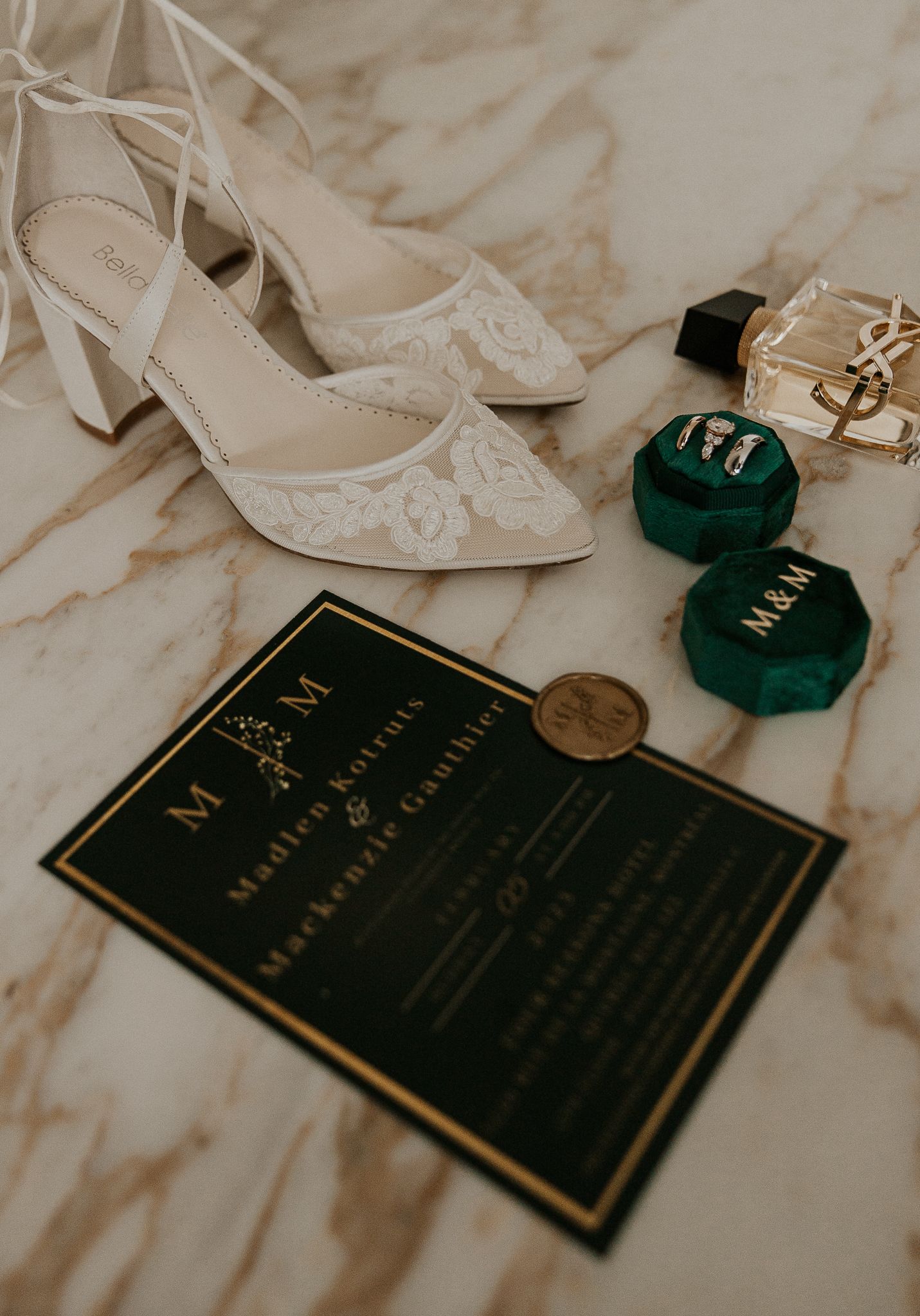 Elegant wedding flat lay with lace bridal heels, green velvet ring boxes, gold wax seal invitation on marble.