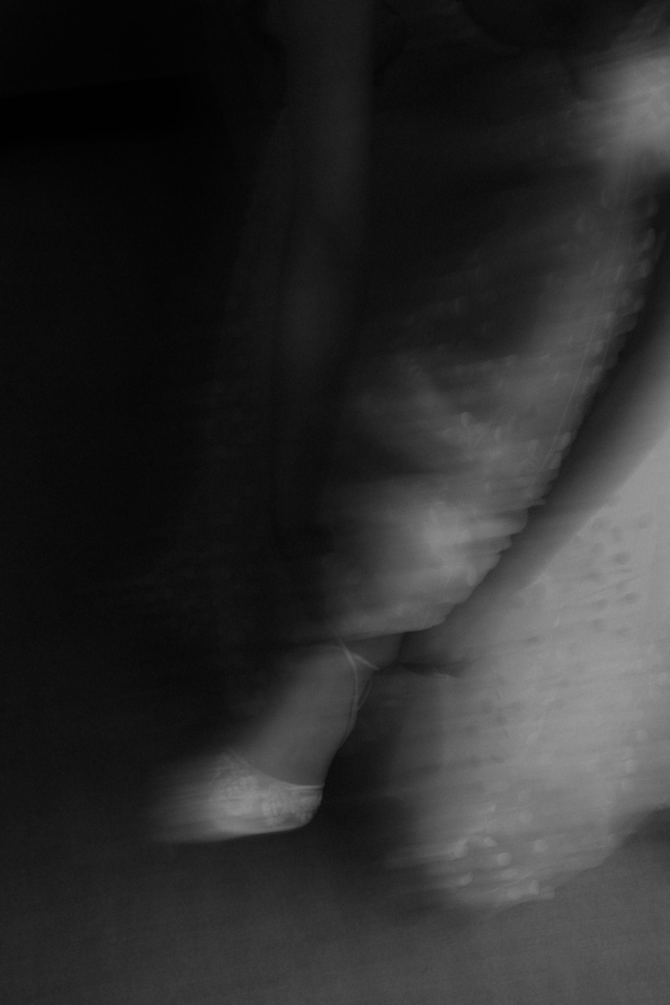 Abstract black and white motion blur photo of bride's wedding dress and heels.