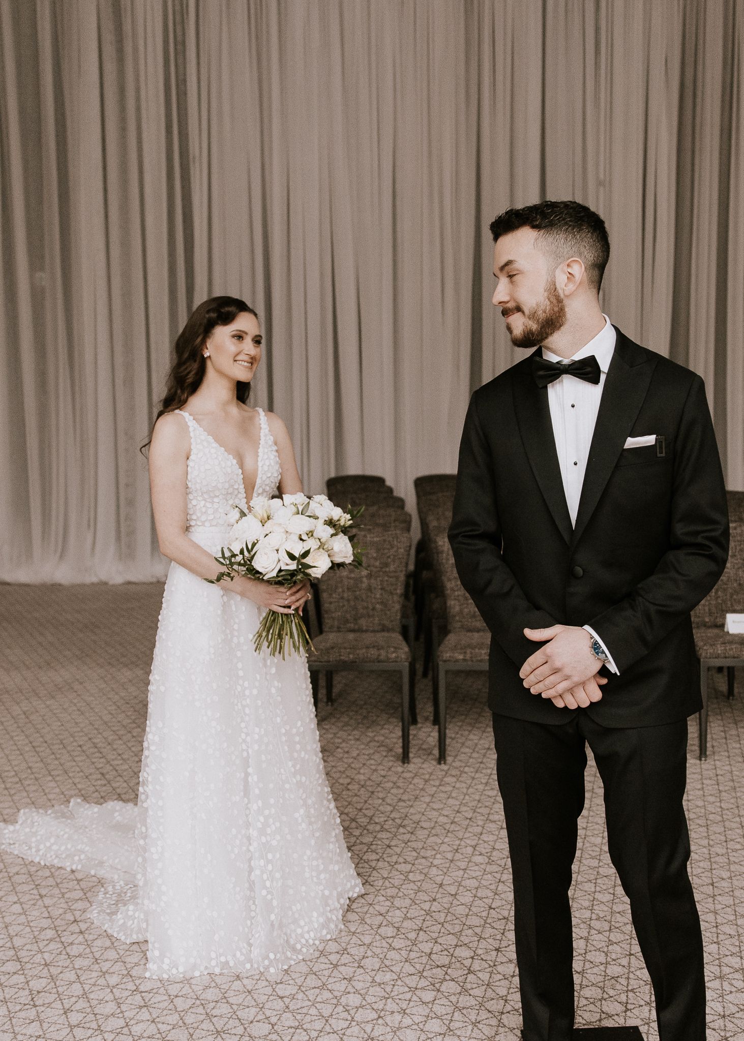 Bride in pearl wedding gown and groom in tuxedo smiling during first look reveal.