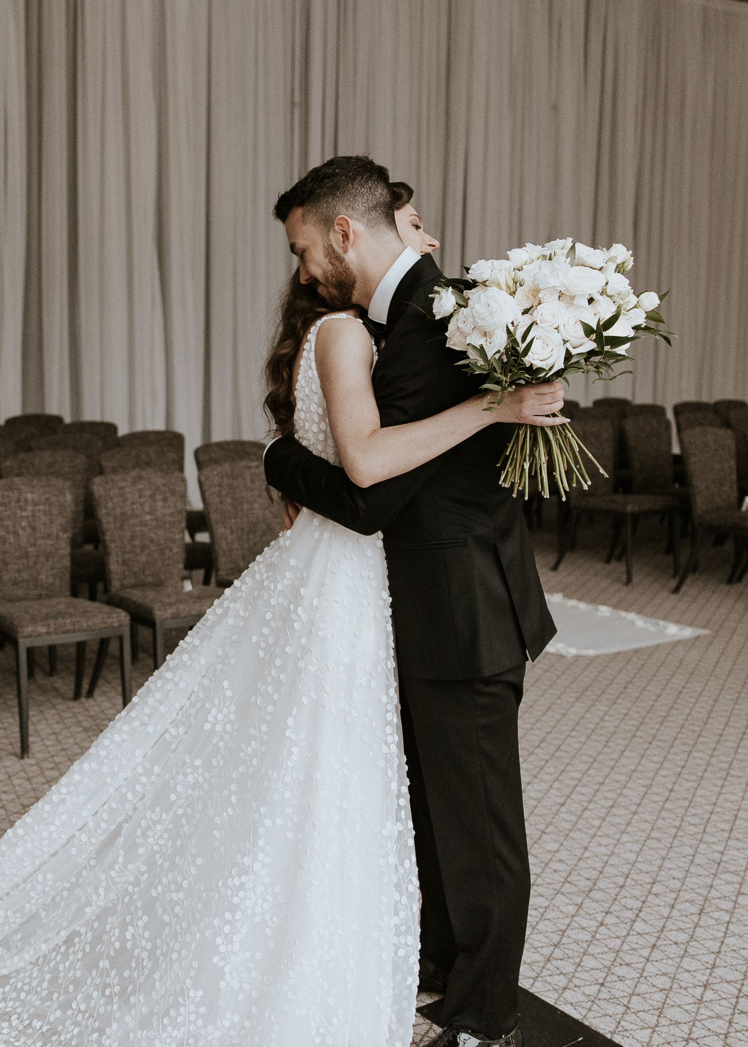 Bride and groom sharing emotional first look embrace holding white rose bouquet at wedding.