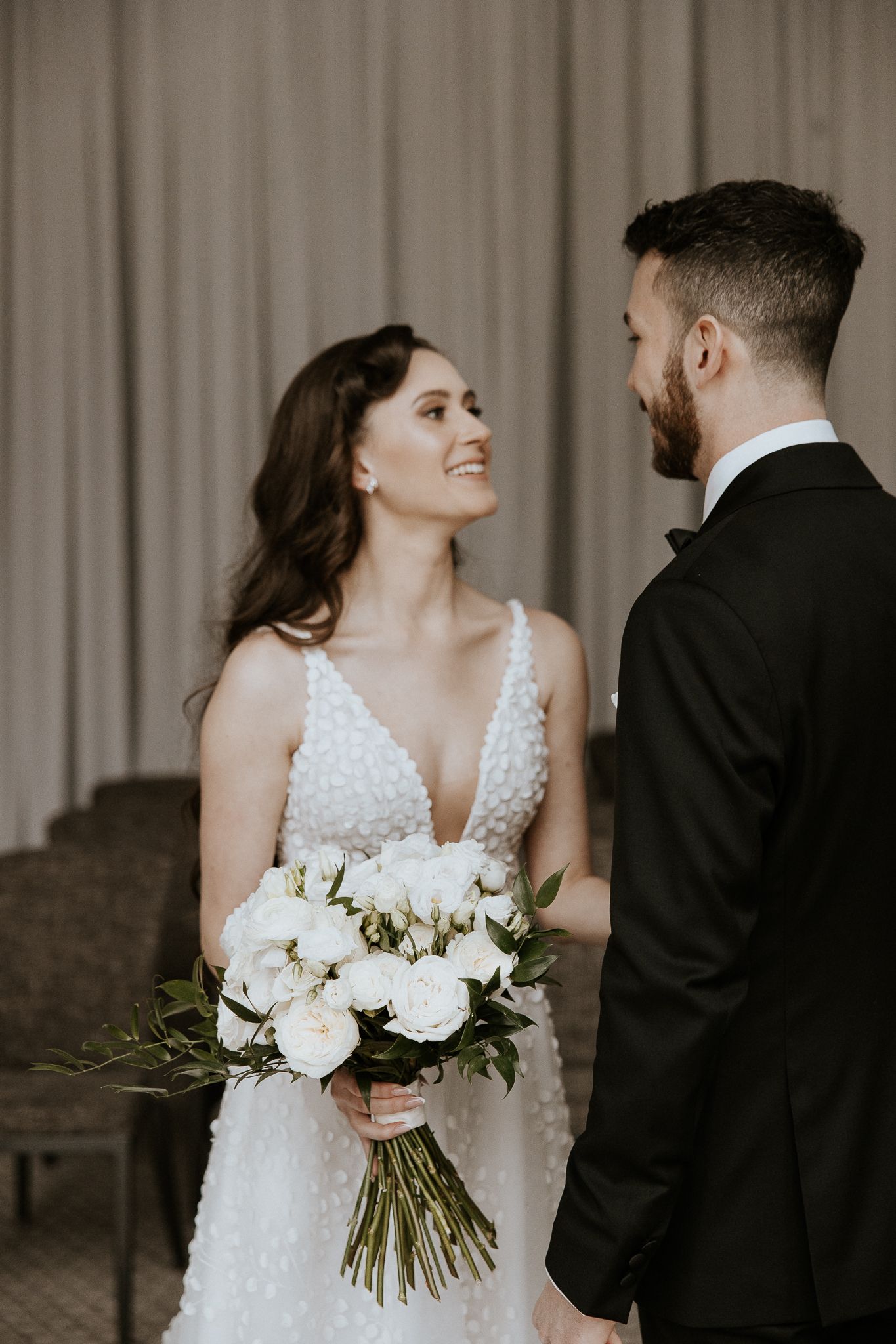 Radiant bride in pearl-embellished gown gazes at bearded groom during romantic first look ceremony.