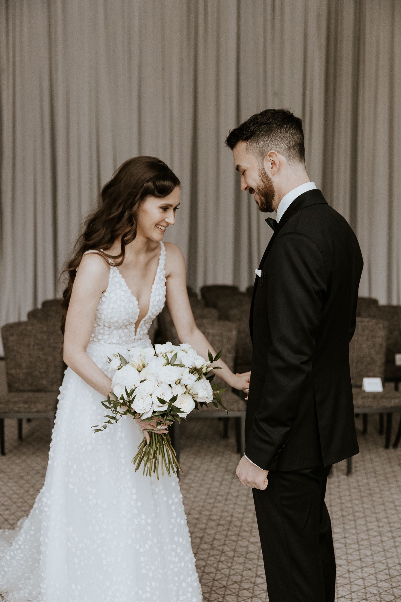 Smiling bride and groom share tender first look moment, bride holding elegant white peony bouquet.