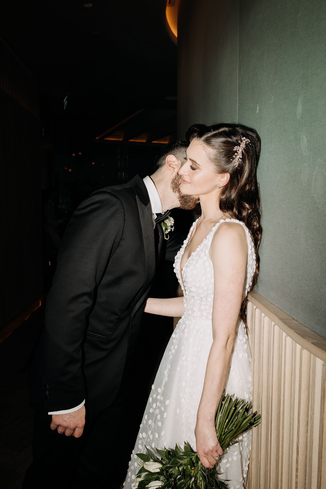 Bride and groom sharing a romantic kiss, bride holding white bouquet in elegant wedding attire.