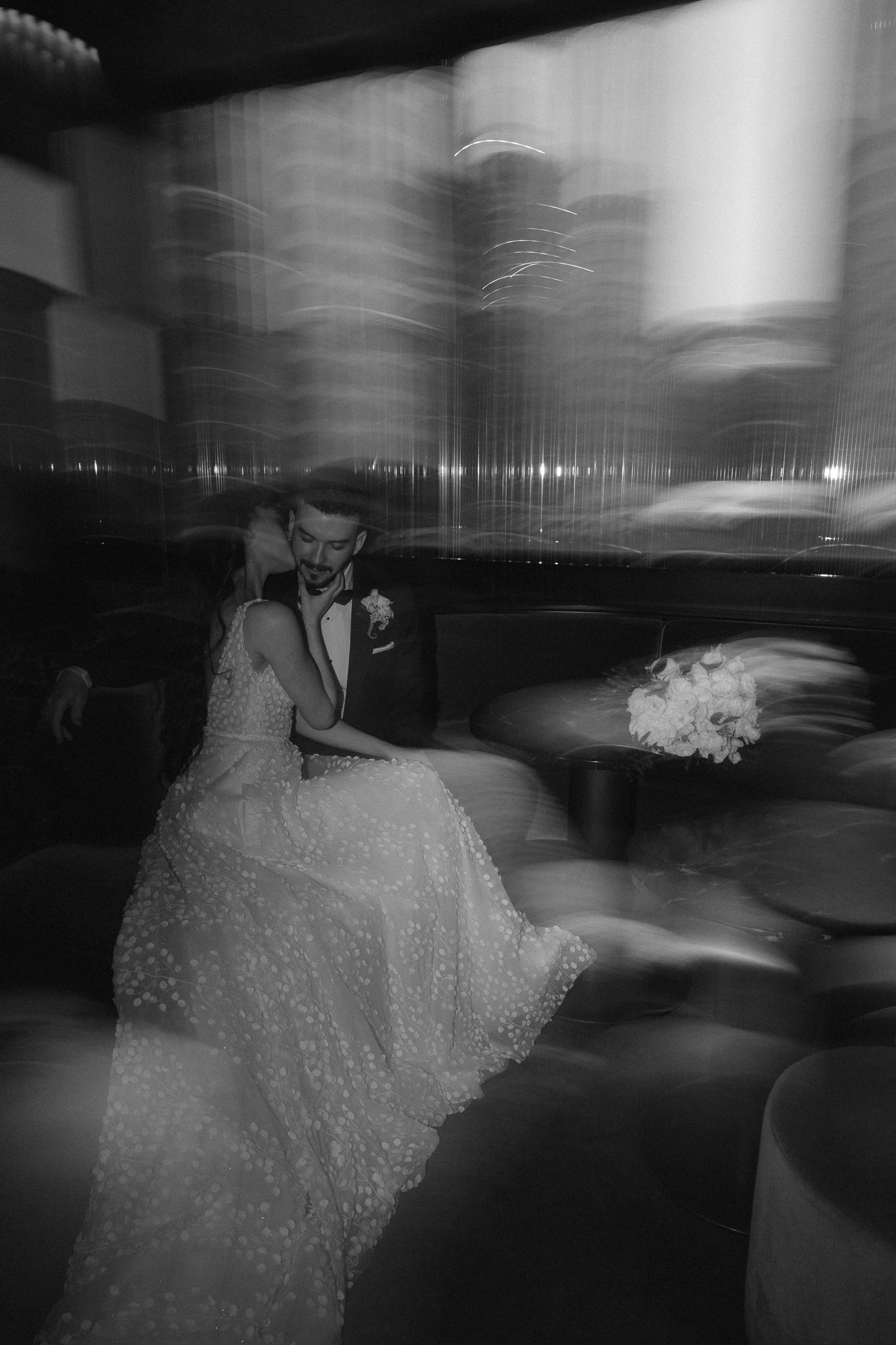 Artistic black and white motion blur photo of bride and groom seated together at wedding reception.