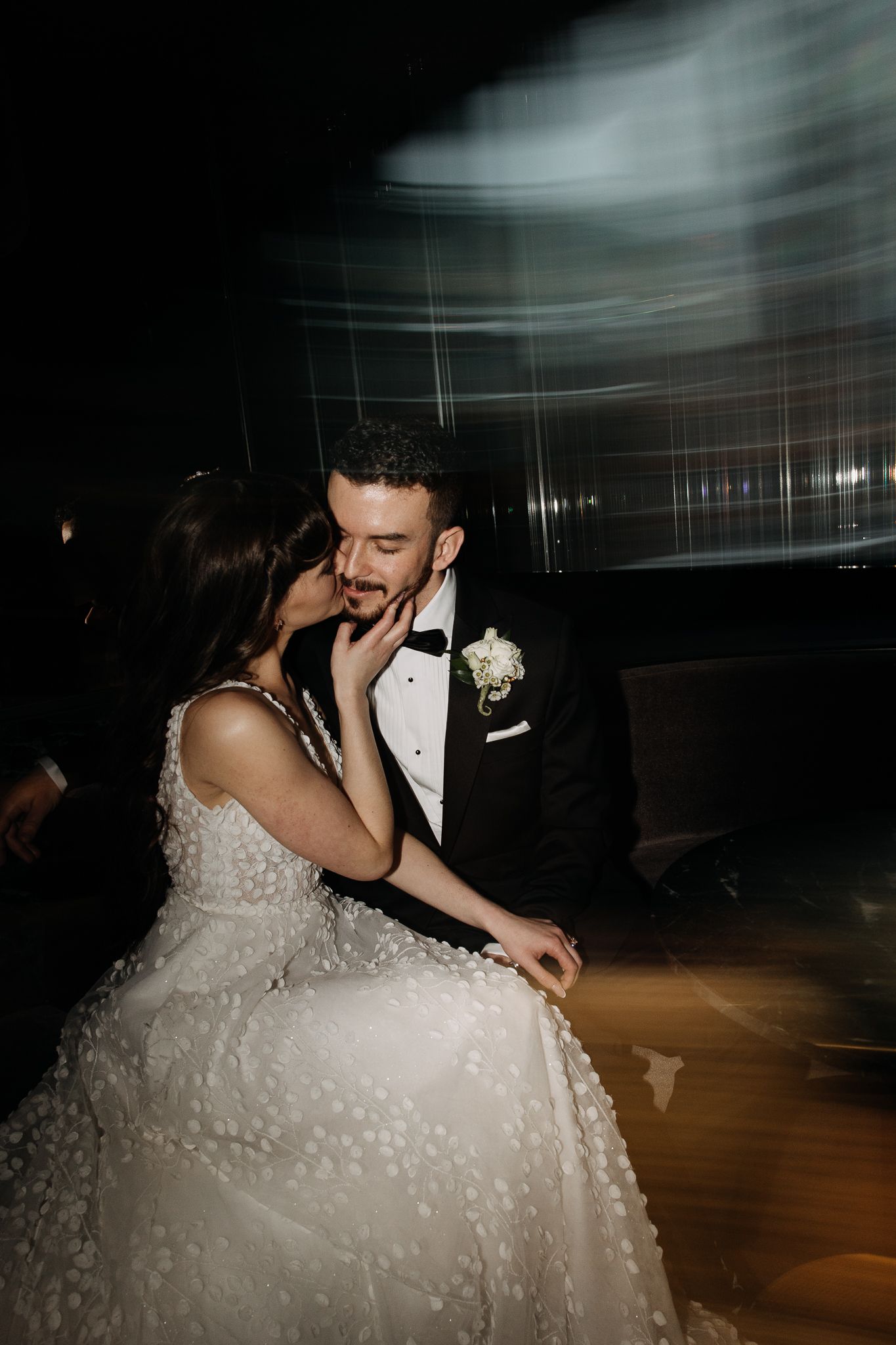 Bride kissing groom's cheek during first dance captured with artistic motion blur photography.