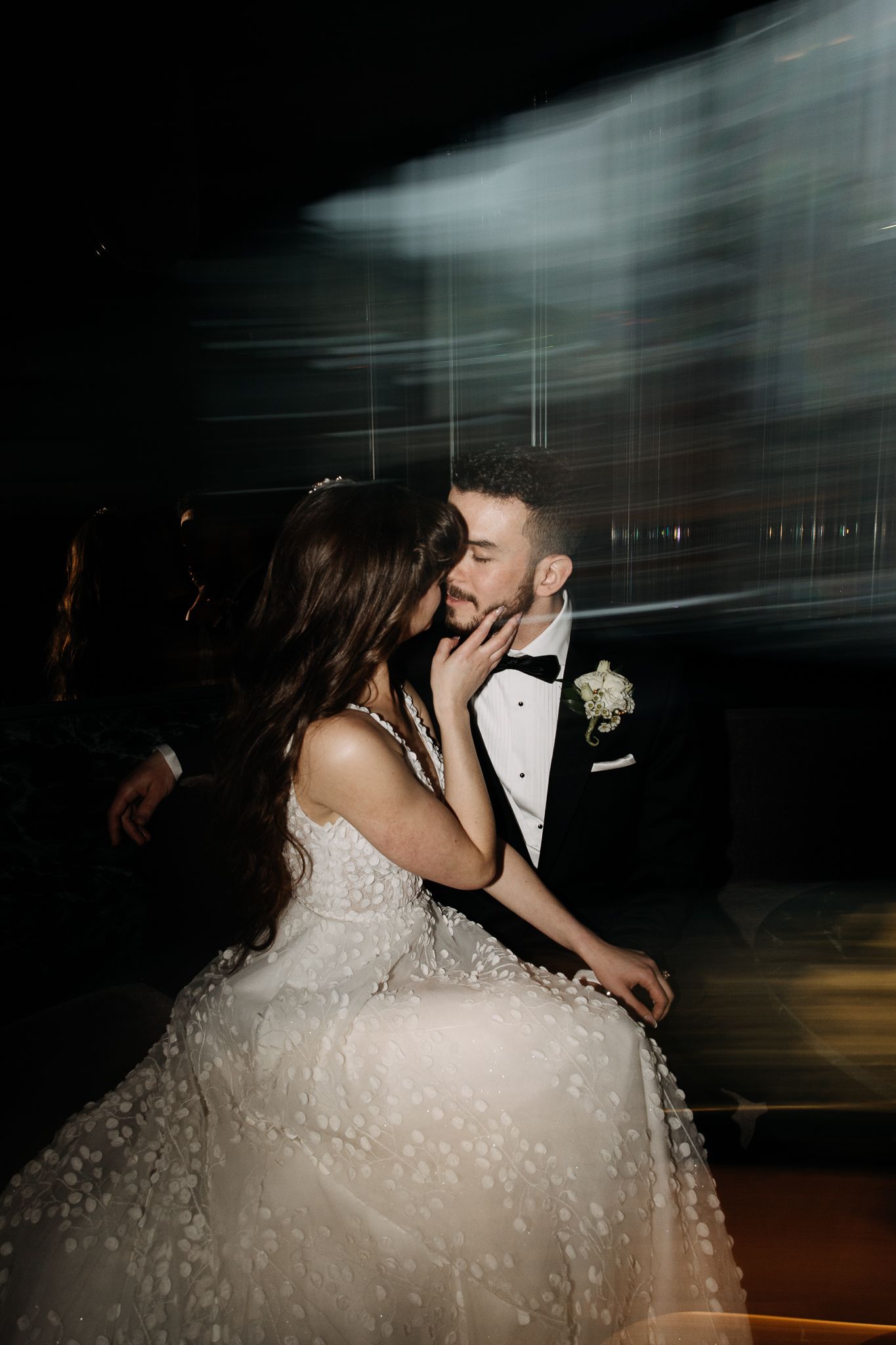 Bride tenderly holds groom's face during romantic first dance with dramatic motion blur effect.