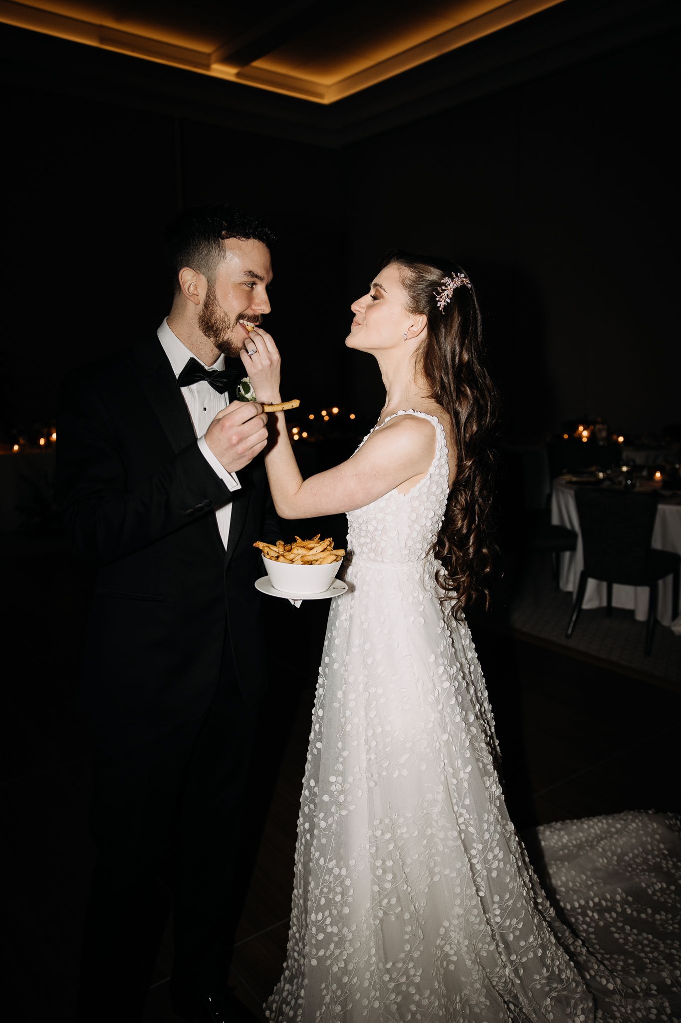 Bride feeding groom french fries in a playful and fun wedding reception moment.