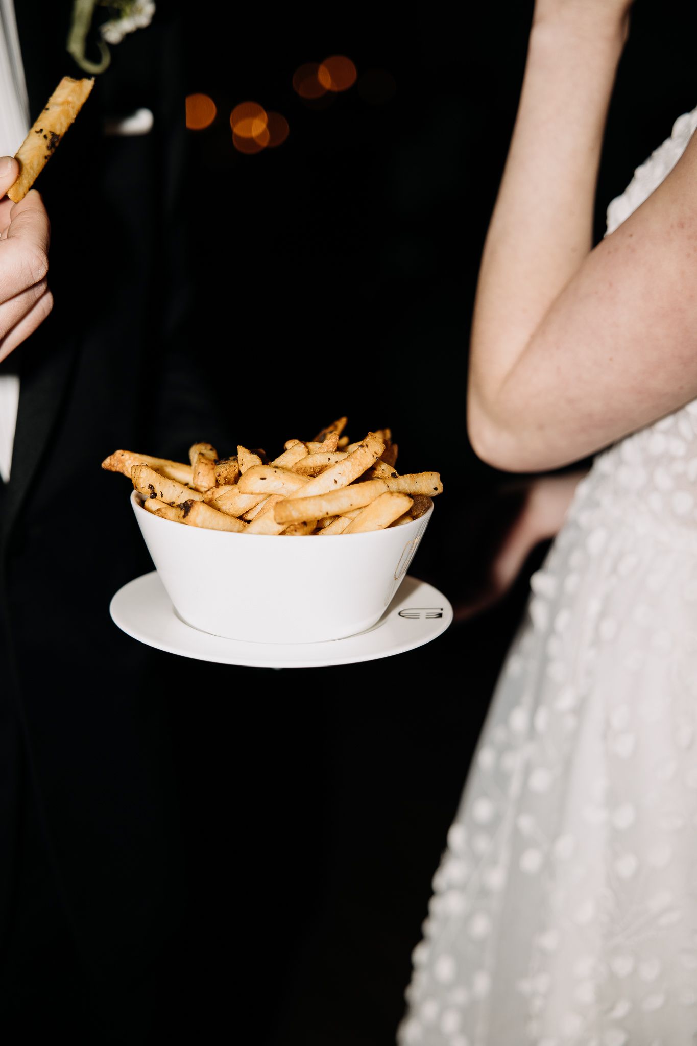 Close-up of a white bowl filled with golden french fries at a wedding reception.