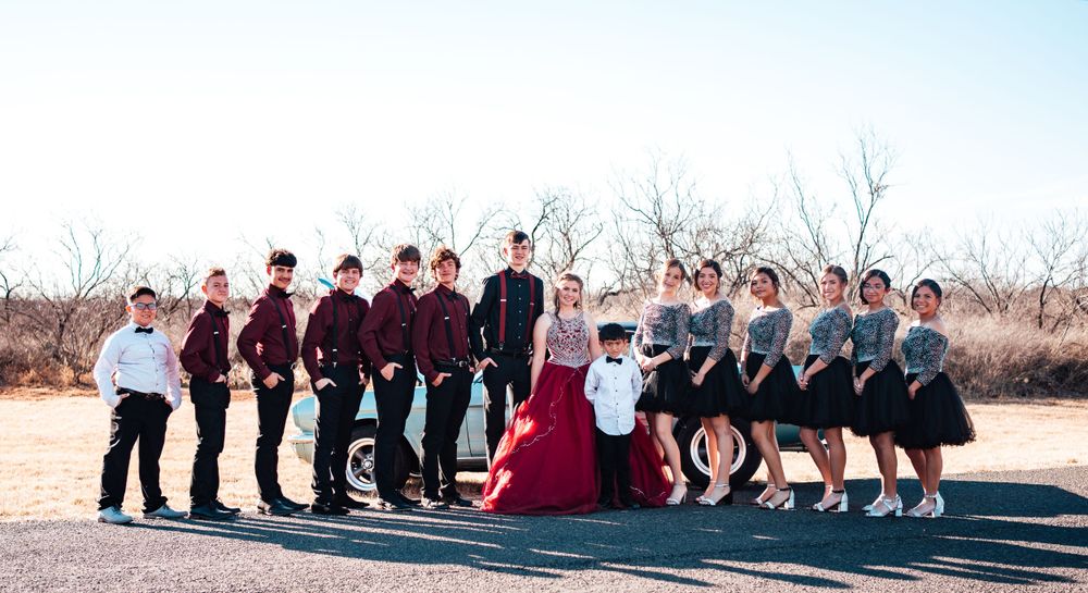 Large group photo lineup in desert with classic car visible in background.