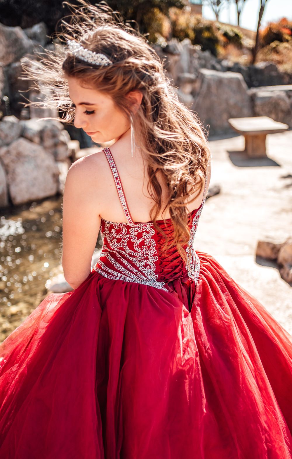 A flowing red ballgown with intricate white beaded details on the bodice sparkles in golden sunlight.