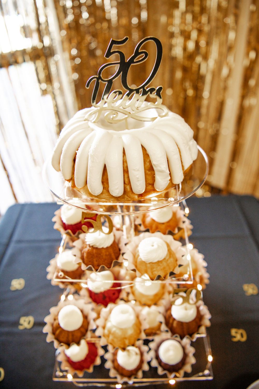 A tiered cake display with white frosting and gold number toppers for a 50th celebration.