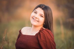 Portrait in soft autumn lighting featuring a burgundy top against a warm blurred background.