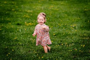 A small child in a floral dress runs joyfully through a grass field dotted with yellow flowers.