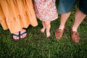 Close-up of three pairs of feet standing together on green grass, showing casual summer footwear.