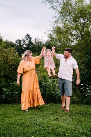A playful moment in a garden as three people swing a small child in a floral dress.