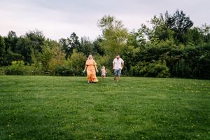 Two people in casual attire walking across a peaceful hilltop meadow against a tree-lined backdrop.
