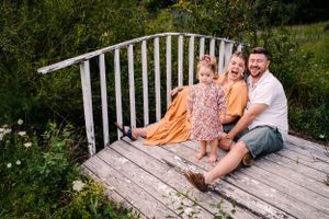 A cheerful family portrait on a weathered wooden bridge deck surrounded by summer greenery.
