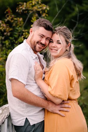 A loving embrace captured against lush summer foliage on a rustic wooden bridge.