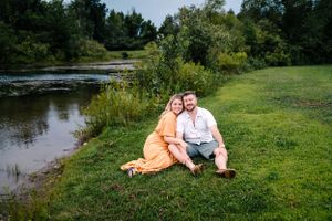 A romantic couple's portrait by a serene pond with lush green surroundings.