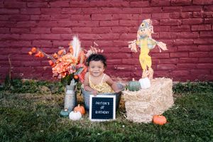Fall themed birthday setup with pumpkins and flowers against a red brick wall.