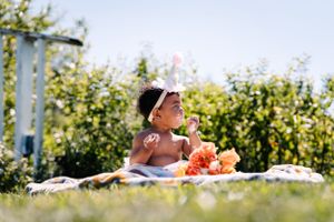 A sunny outdoor picnic scene with flowers and a white blanket on the grass.
