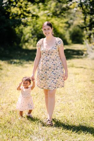 A summer outdoor scene with two people in floral dresses walking through a sunny meadow.