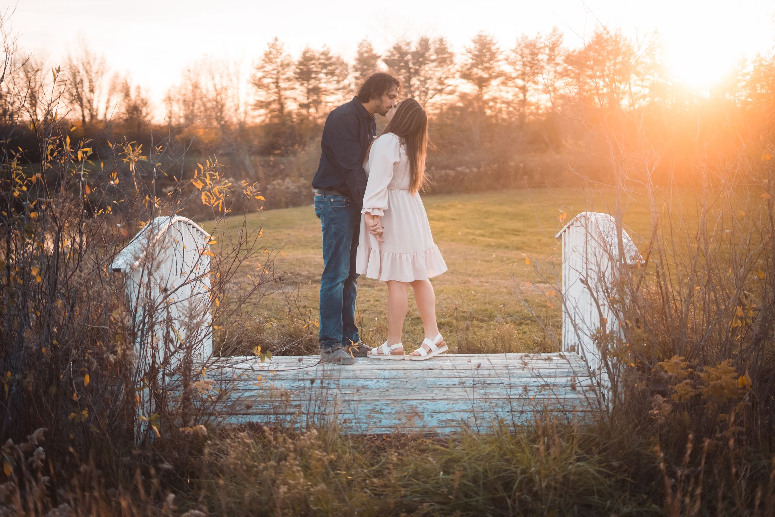 A couple standing on a rustic bridge during a beautiful sunset.