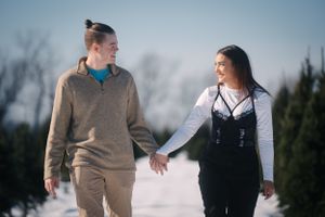 Two people holding hands while walking through a snowy winter landscape.