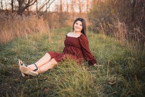 A burgundy-dressed figure reclines in tall autumn grass during a golden hour photoshoot.