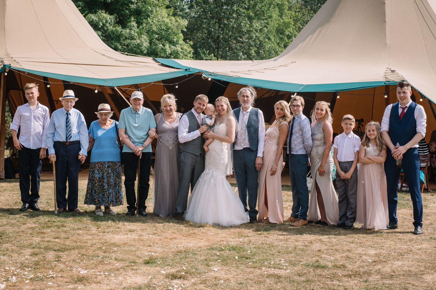 Large group wedding photo with guests lined up outside rustic tent venue.
