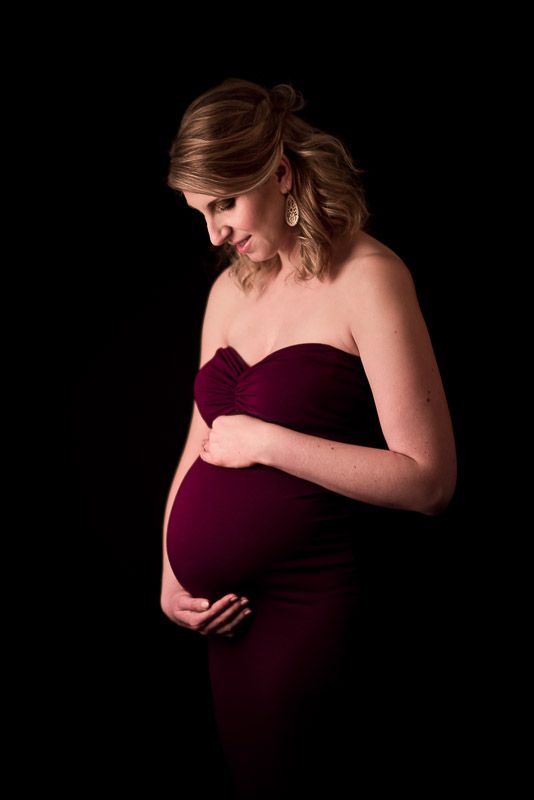 zwangere vrouw tijdens fotoreportage in studio met handen op de buik