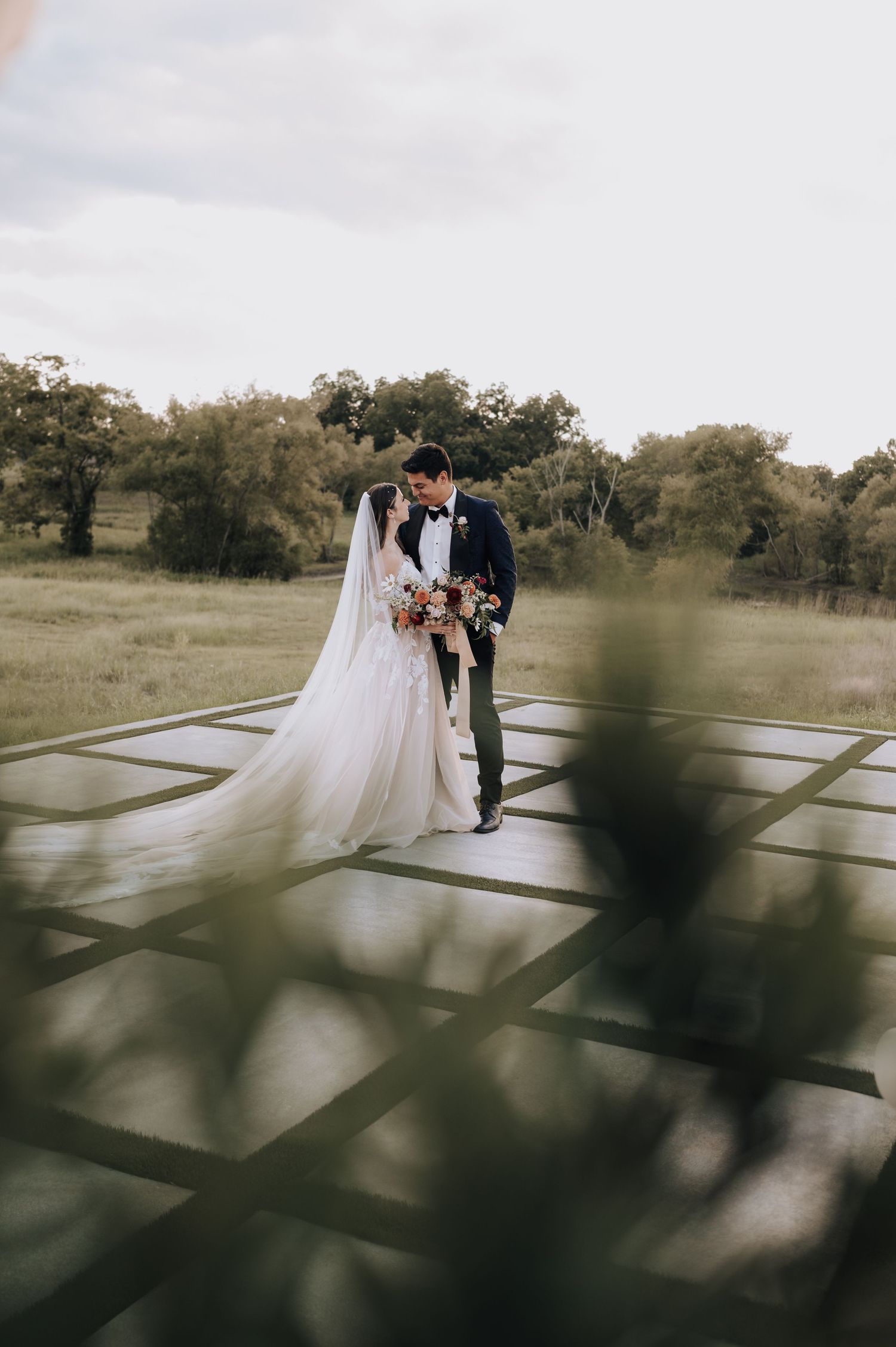 Artistic wedding portrait on geometric platform surrounded by dreamy outdoor landscape.