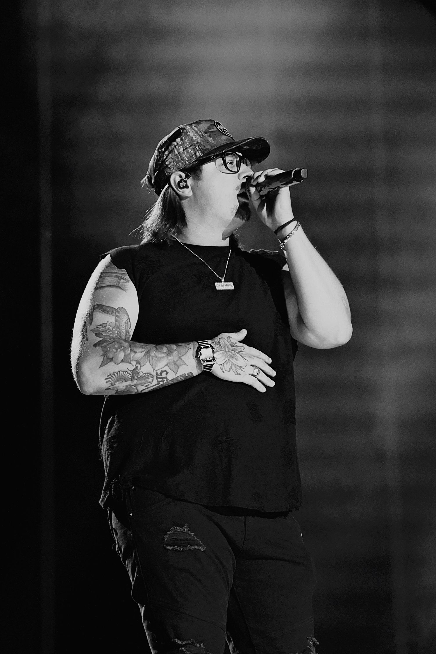 Black and white concert photo of performer in dark attire on stage.