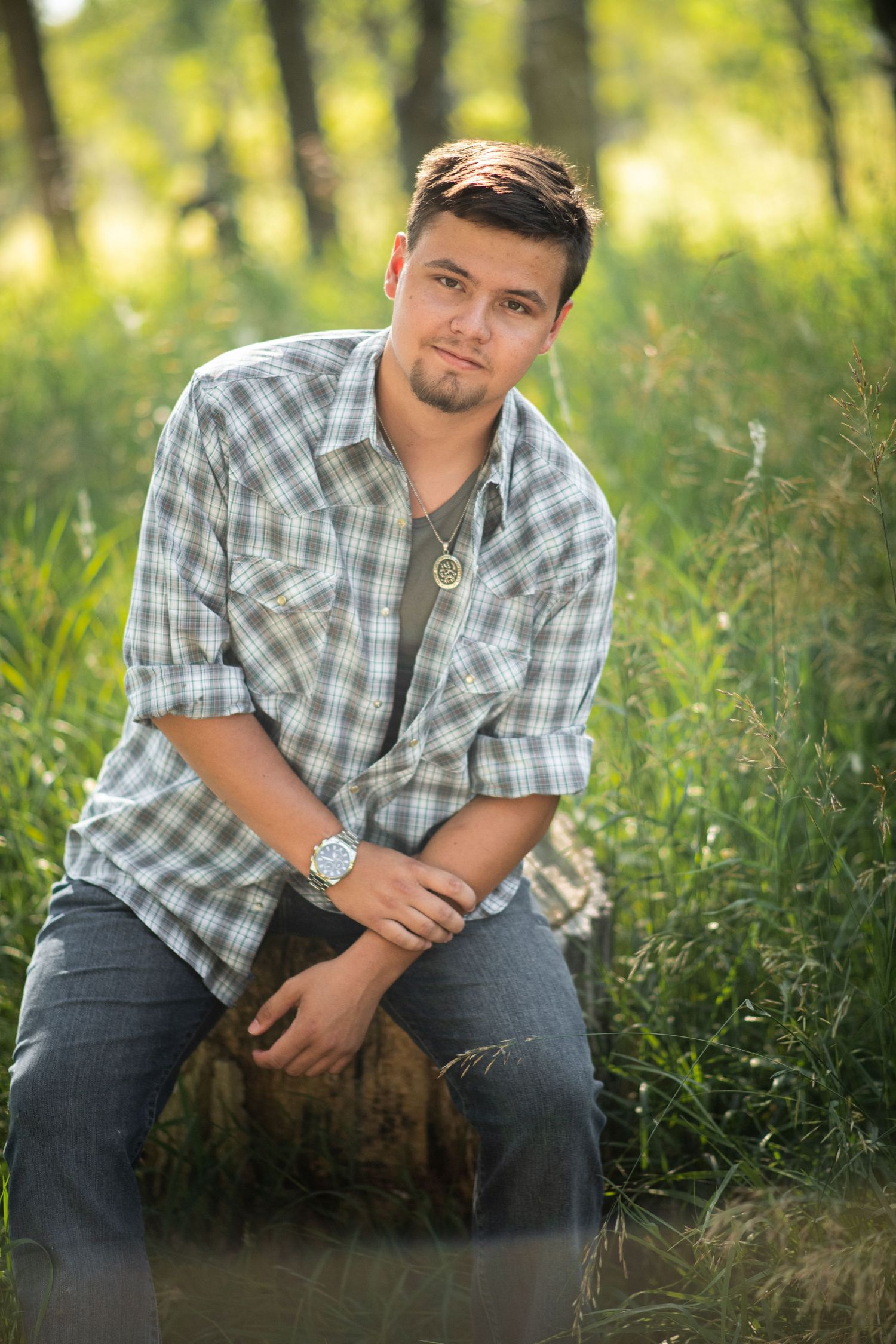 Portrait of person in plaid shirt sitting on log in sunlit forest setting.
