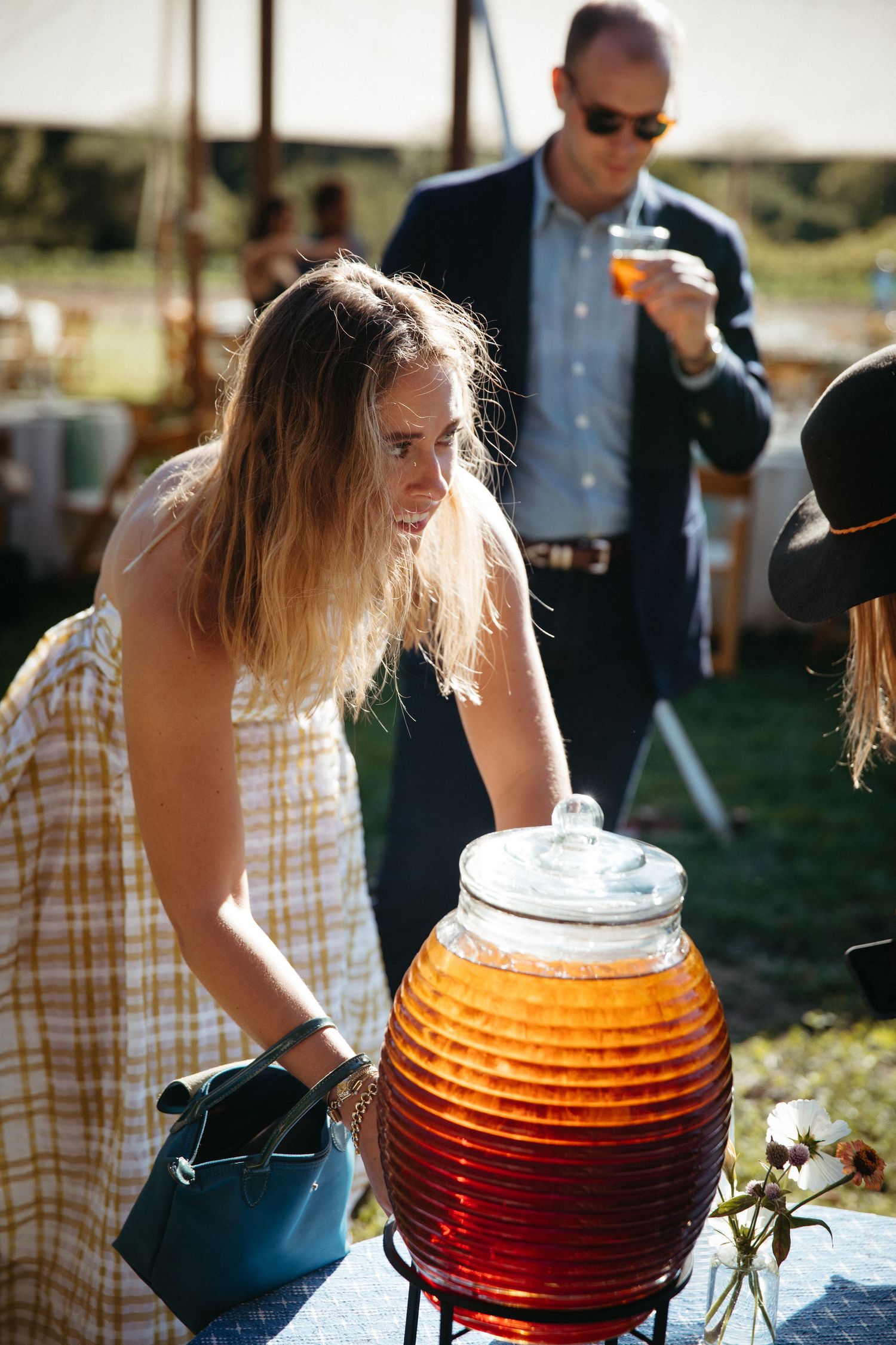 Person serving from a large decorative beverage dispenser at an outdoor event.