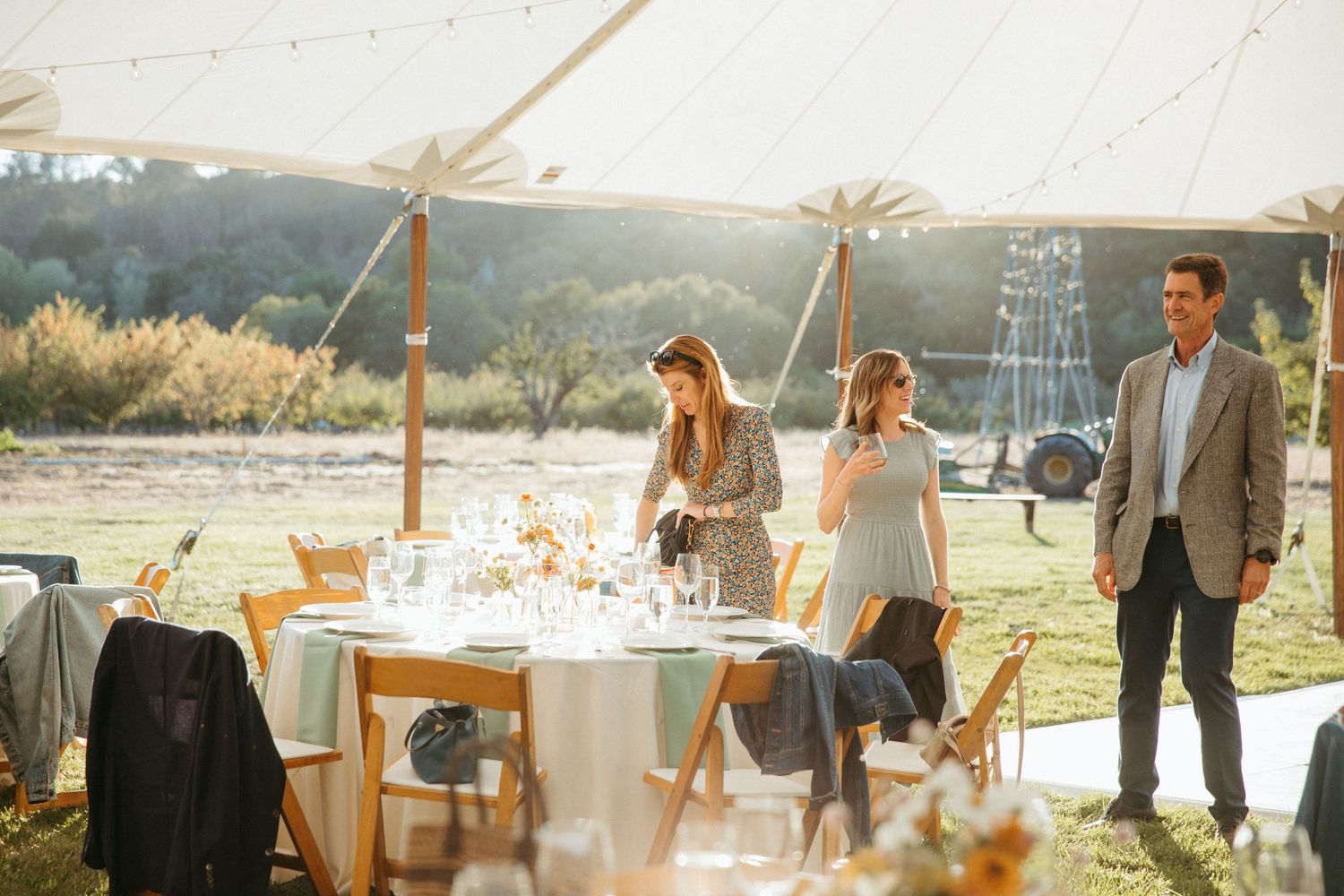 Elegant outdoor wedding reception setup with tables under a tent at sunset.