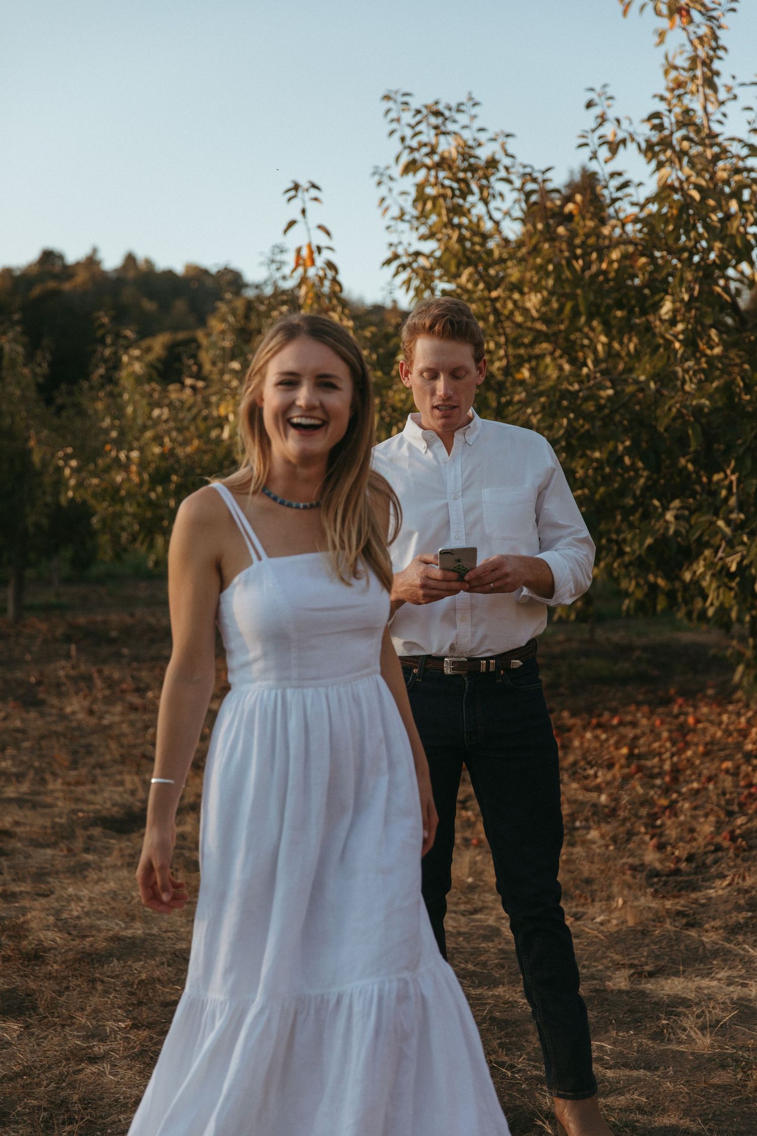 White wedding tent set up in field with couple viewing from distance.