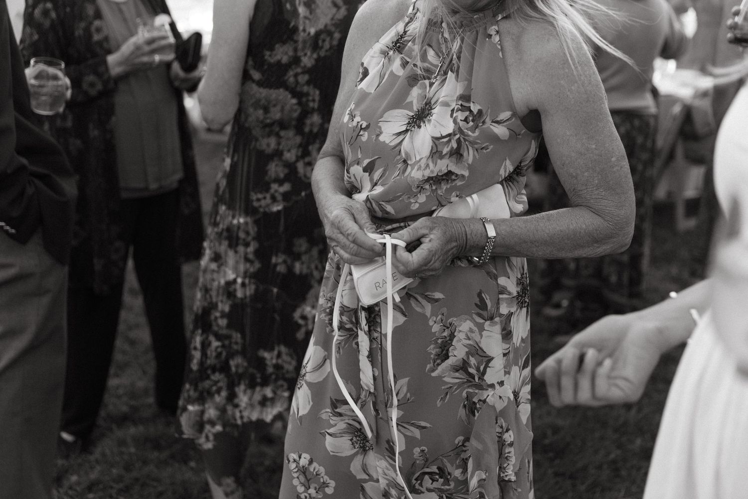 Someone in a floral dress holding a drink at an outdoor gathering.