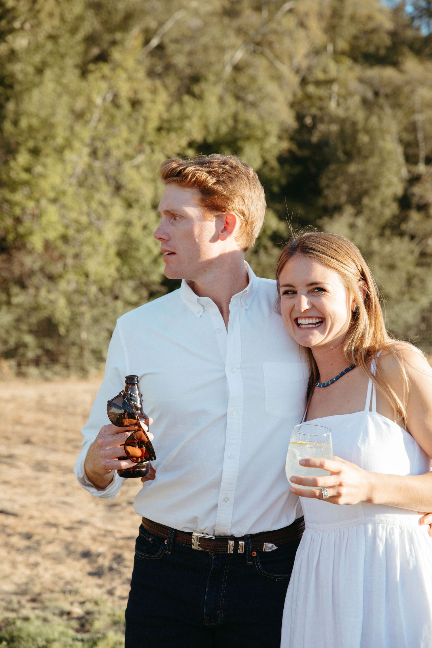 A couple shares drinks and laughter at a sunny outdoor event.