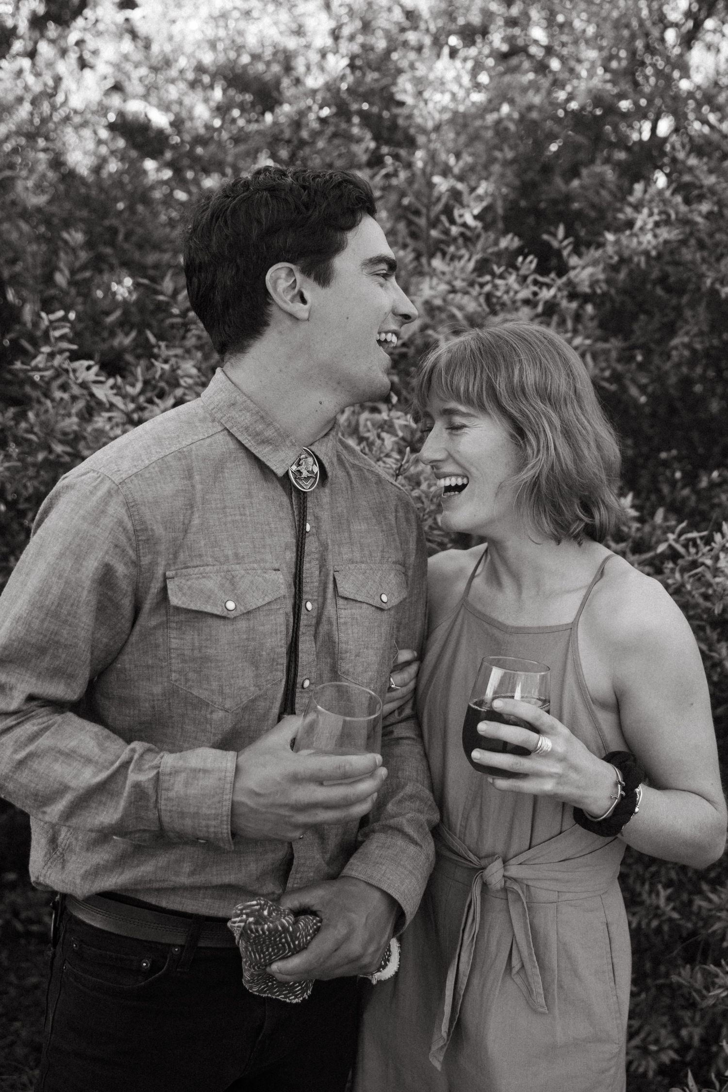 A couple shares a laugh while holding drinks outdoors.