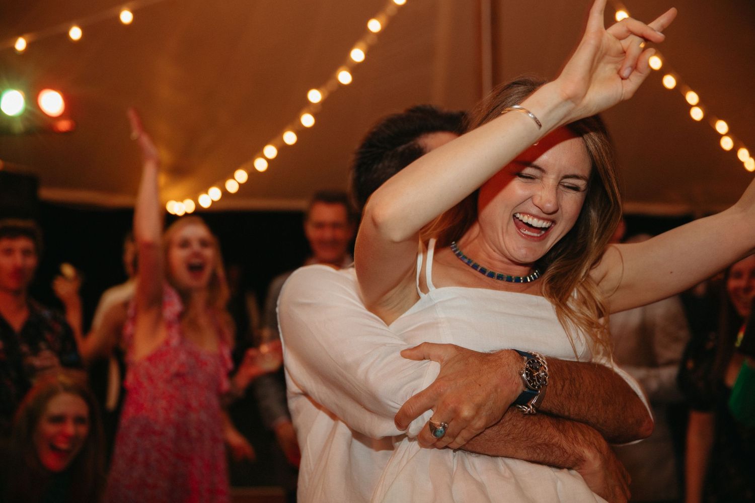 Joyful dancing at a wedding reception under warm string lights creates a festive atmosphere.
