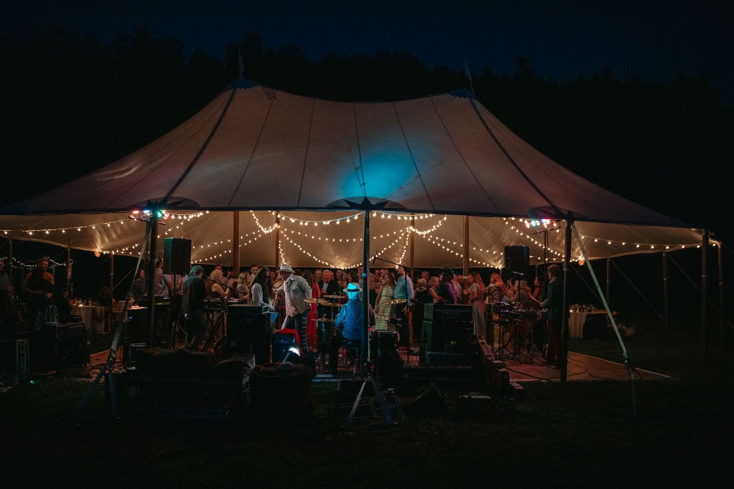 Large wedding tent illuminated at night with string lights and blue uplighting.