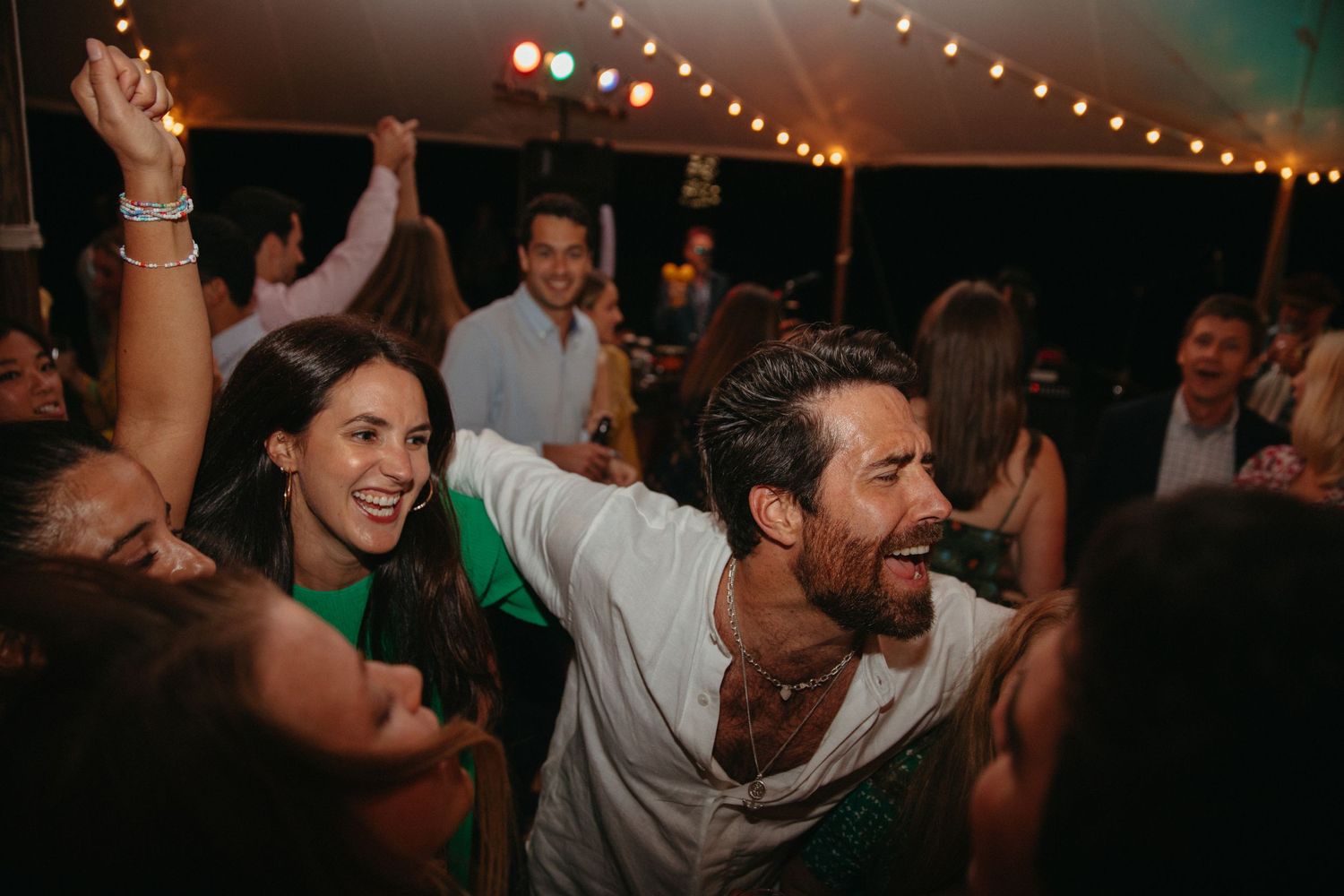 Energetic crowd dancing and celebrating at nighttime party under tent lighting.